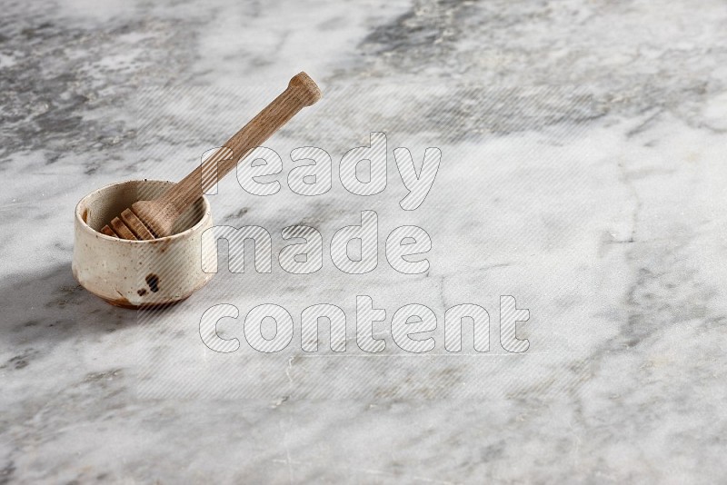 Beige Pottery Bowl with wooden honey handle in it, on grey marble flooring, 45 degree angle