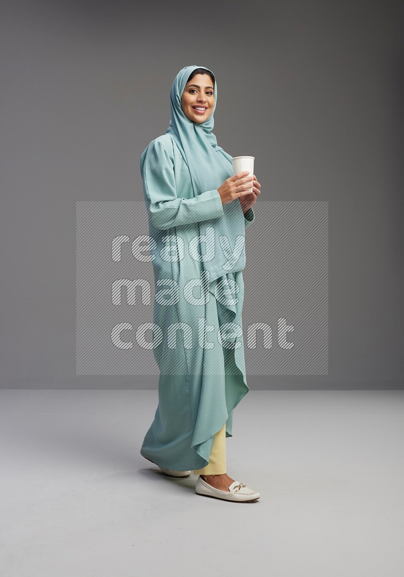 Saudi Woman wearing Abaya standing  holding paper cup on Gray background