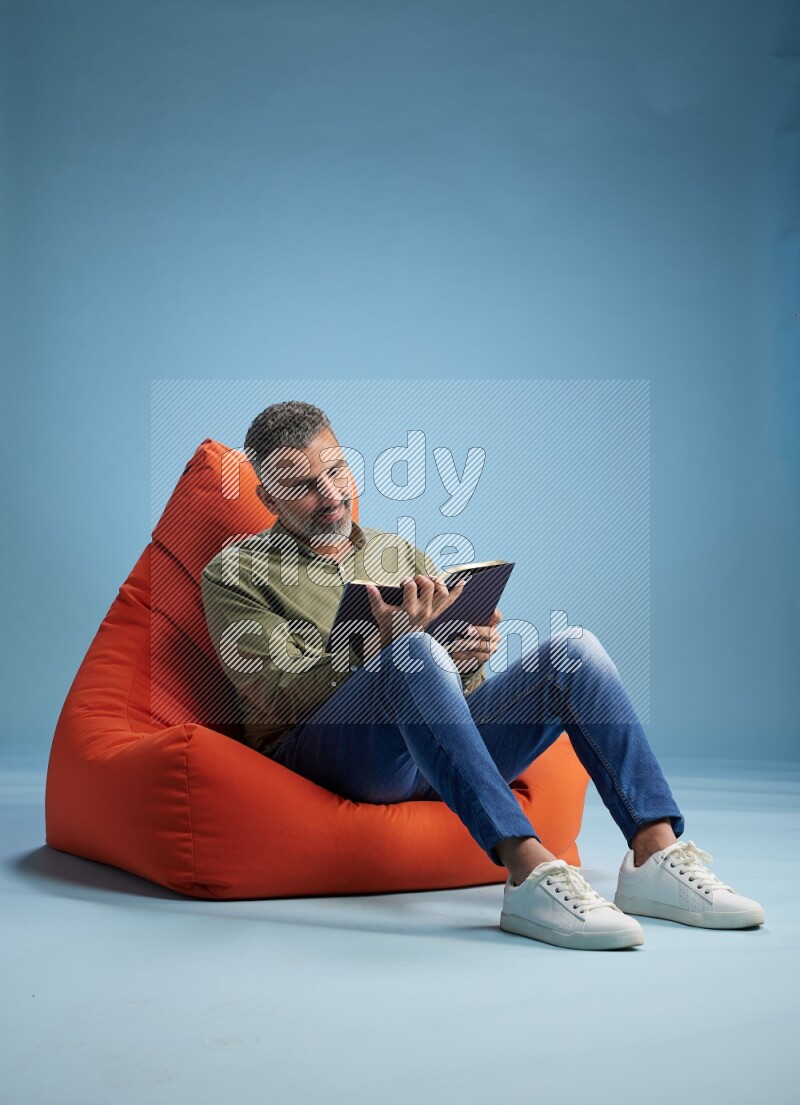 A man sitting on an orange beanbag and reading a book