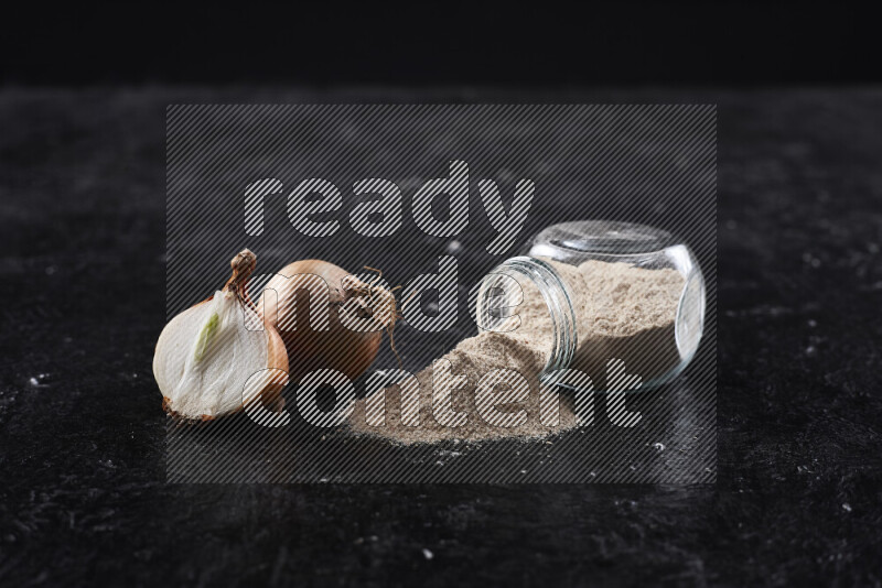 A glass jar full of onion powder flipped with some spilling powder on black background