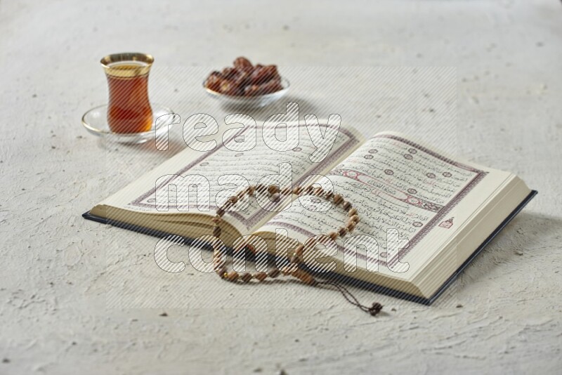 Quran with dates, prayer beads and different drinks all placed on textured white background
