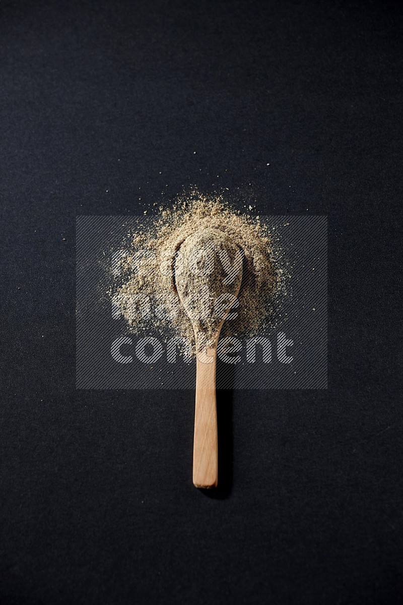 A wooden spoon full of cardamom powder and powder spreaded on black flooring