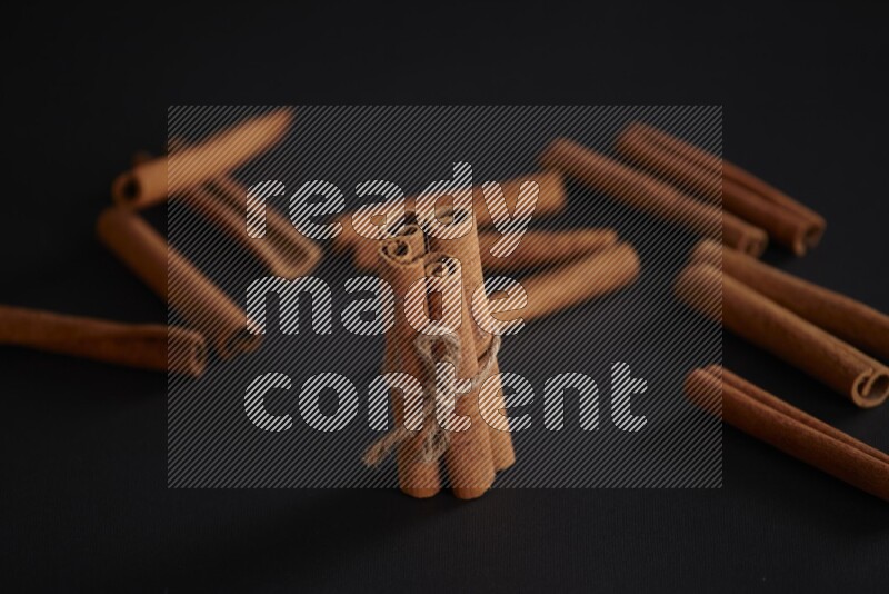 4 Cinnamon sticks stacked and bounded with more sticks in the background on black flooring
