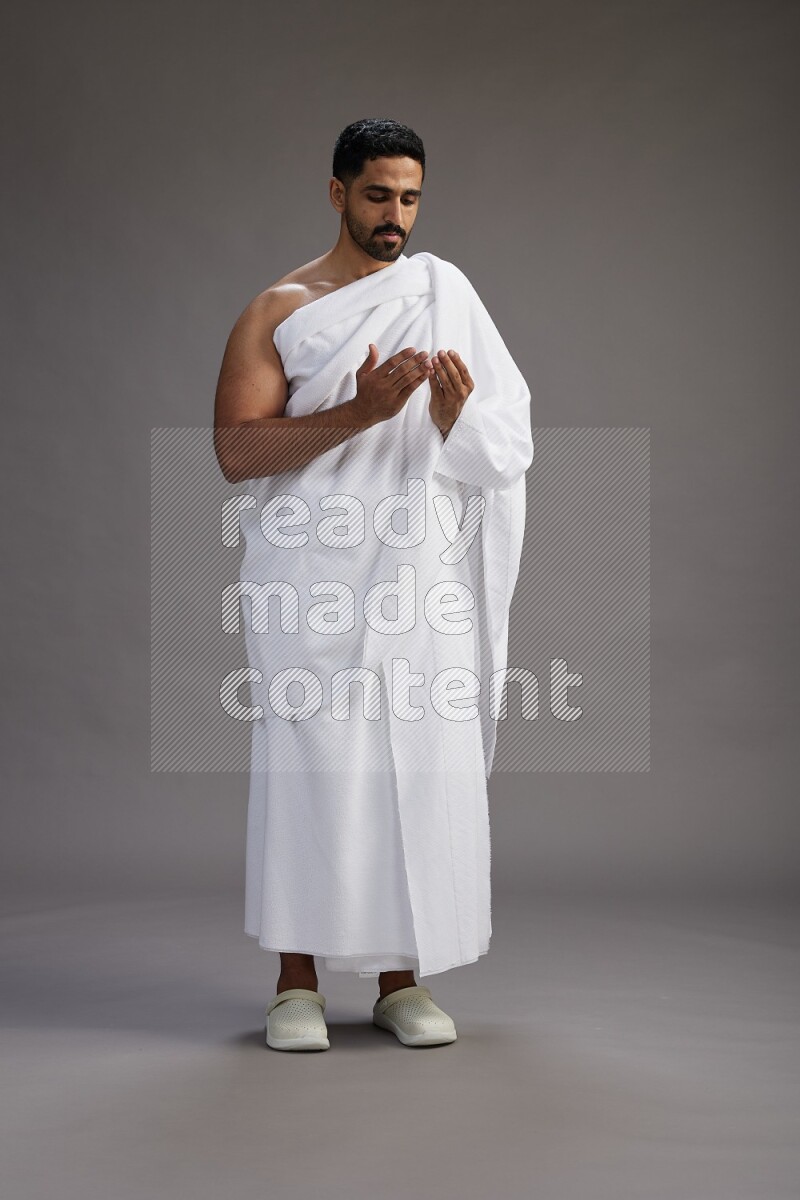 A man wearing Ehram Standing performing dua'a on gray background