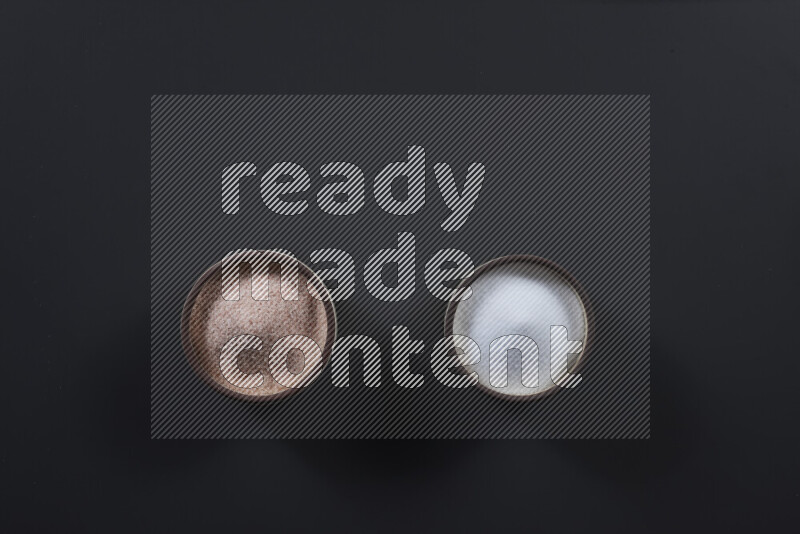 2 وعاء فخاري احدهمها ممتلئ بملح الهيمالايا والأخر بالملح الأبيض على خلفية سوداء