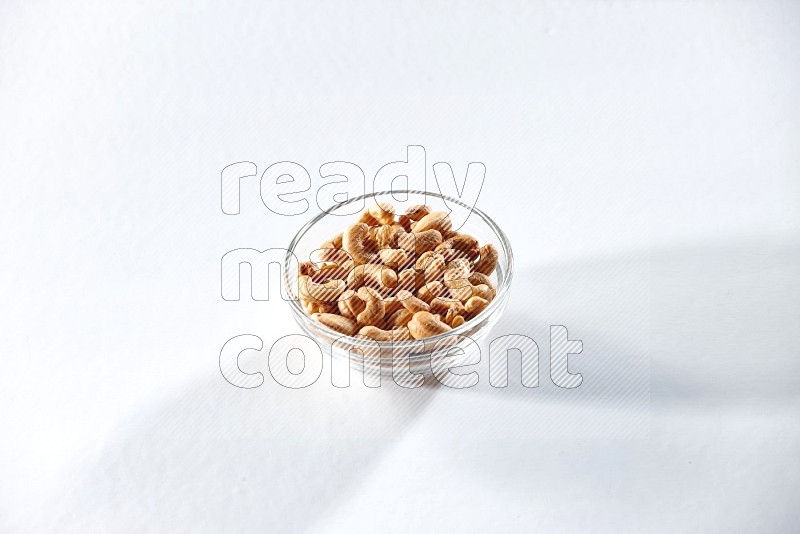 A glass bowl full of cashews on a white background in different angles
