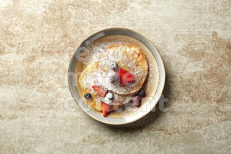 Three stacked mixed berries pancakes in a bicolor plate on beige background