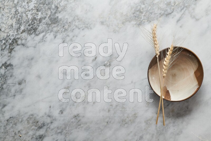 Wheat stalks on multicolored pottery plate on grey marble background