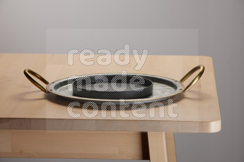 black plate placed on a rounded stainless steel metal tray with golden handels on the edge of wooden table