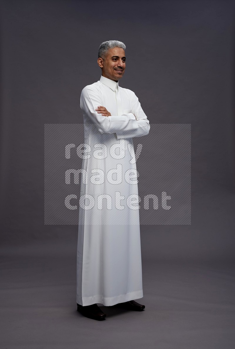 Saudi man wearing thob standing with crossed arms on gray background