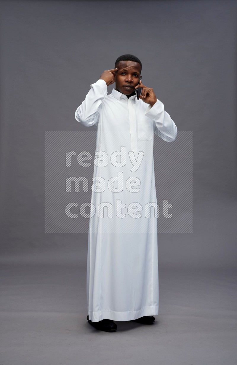 Saudi man wearing thob standing talking on phone on gray background