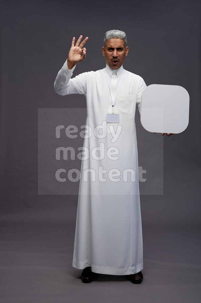Saudi man wearing thob with neck strap employee badge standing holding social media sign on gray background