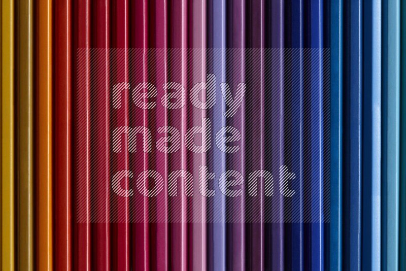 مجموعة من أقلام الرصاص الملونة مرتبة لتعرض تدرجا من الألوان المختلفة علي خلفية رمادية