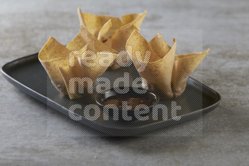wonton cups with soy sauce ramkin on rectangle dark grey ceramic plate on grey textured counter top
