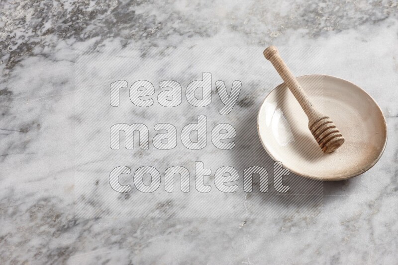 Beige pottery plate with wooden honey dipper in it on grey marble background