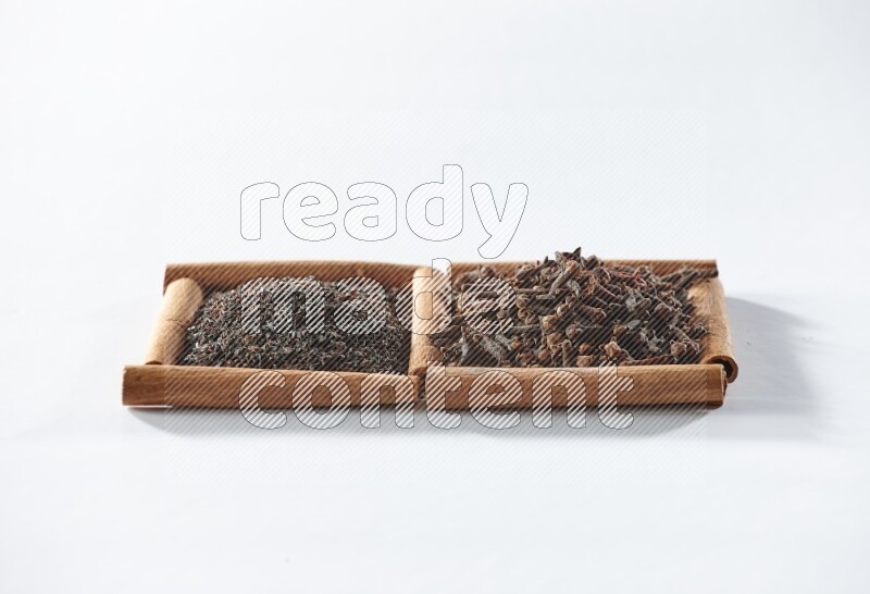 مربعان من أعواد القرفة ممتلئان بالشاي الأسود وحبوب القرنفل علي خلفية بيضاء