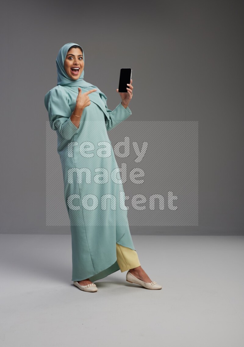Saudi Woman wearing Abaya standing showing phone to camera on Gray background