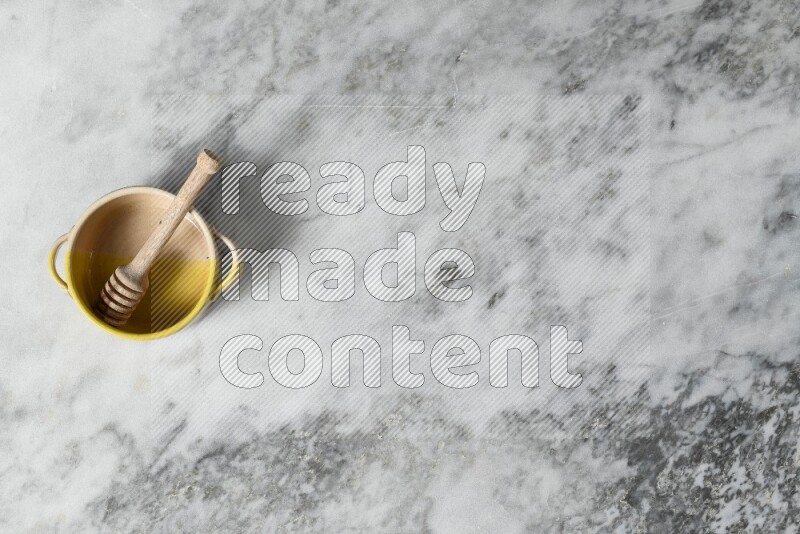 Multicolored pottery bowl with wooden honey dipper in it on grey marble background