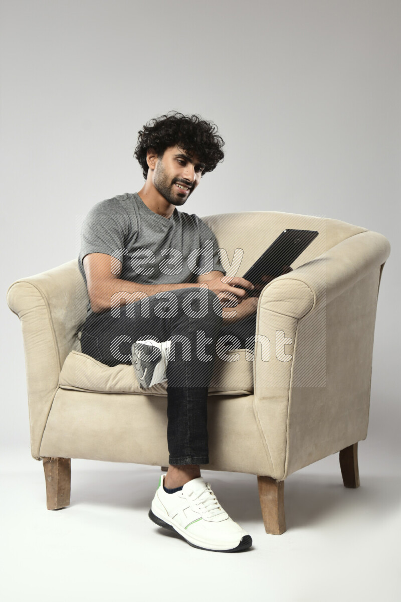 A man wearing casual sitting on a chair browsing on a tablet on white background