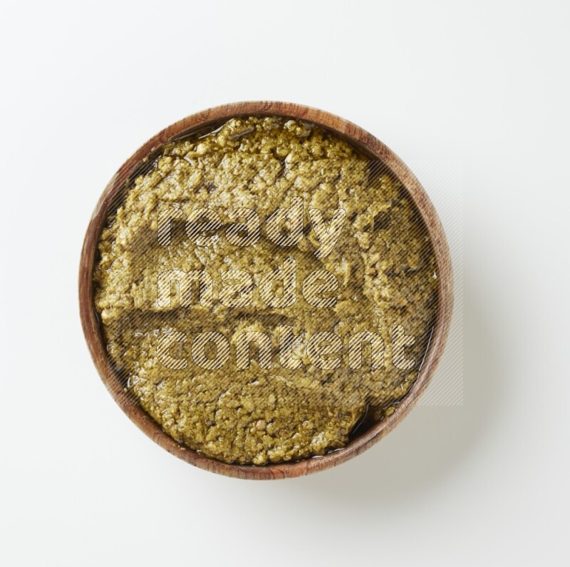 Large brown round wood bowl filled with pesto paste on a white table top