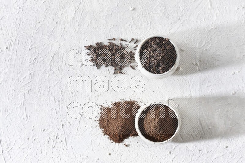 2 Beige ceramic bowls, one full of cloves and the other full of powder on textured white flooring