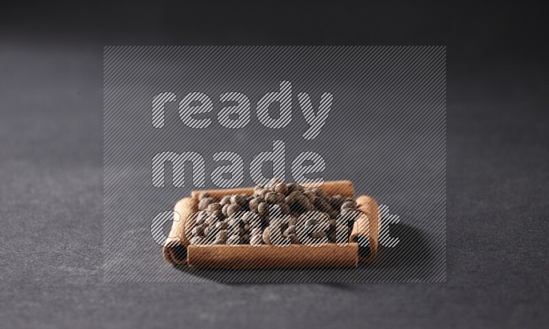 أربعة من أعواد القرفة مكونة شكل مربع بداخلها بهار الفلفل الحلو علي خلفية سوداء