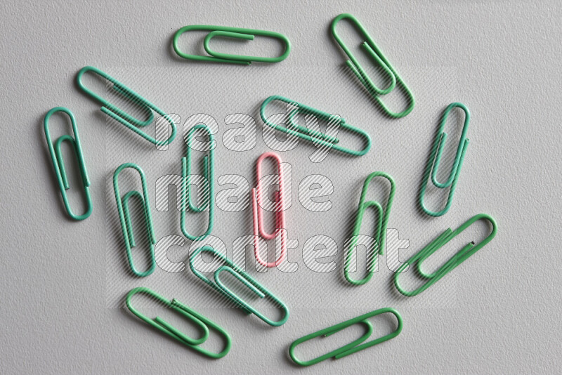 A bunch of green paper clips with a different colored paper clip in the center on grey background
