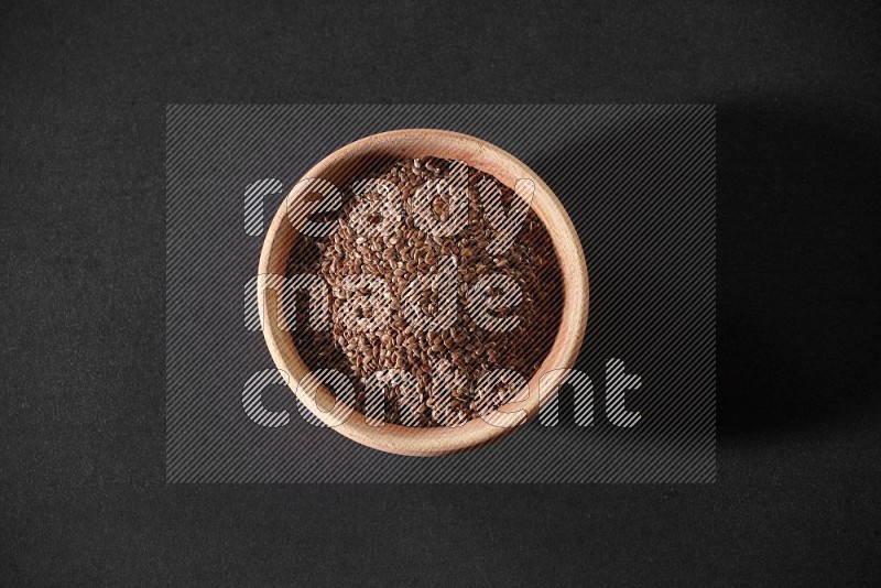 A wooden bowl full of flaxseeds on a black flooring