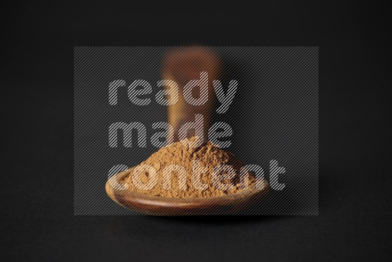 Cinnamon powder in a spoon ladle on black background