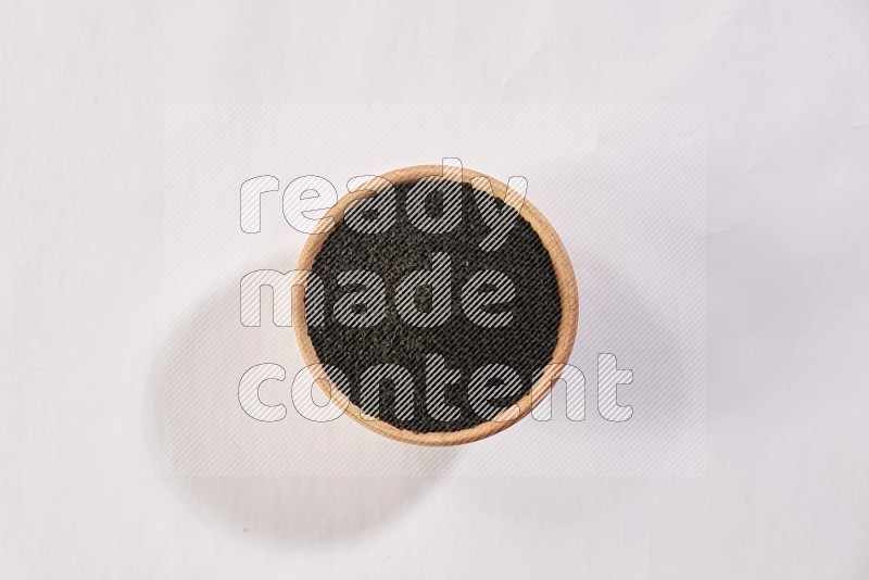 A wooden bowl full of black seeds on a white flooring in different angles