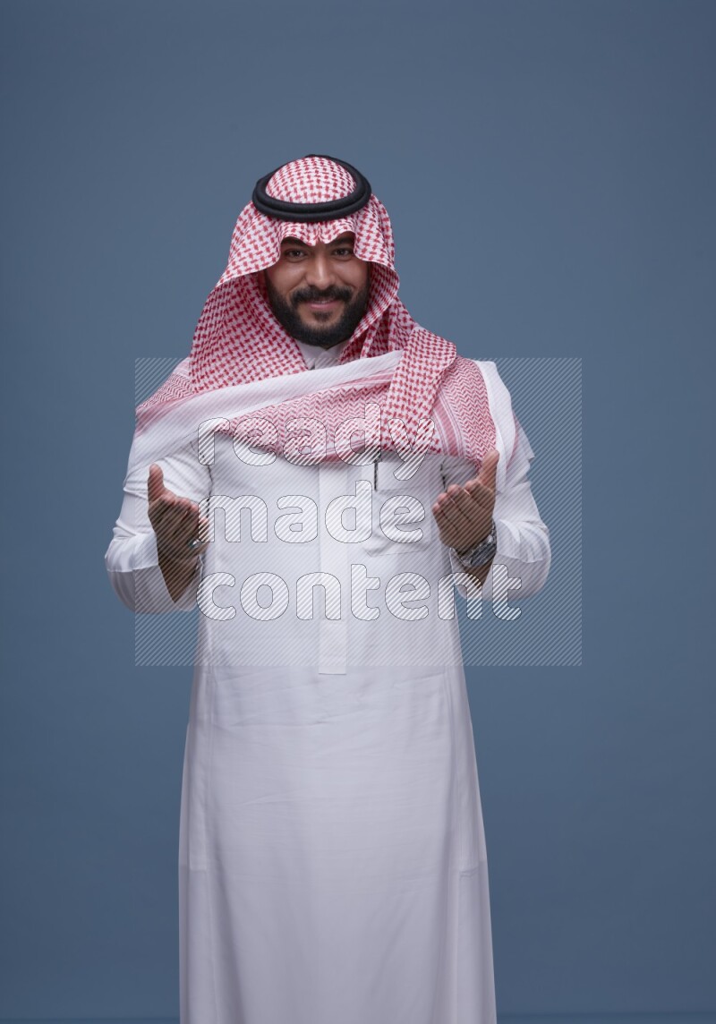 A Saudi man posing on blue background wearing Thob and Shomag