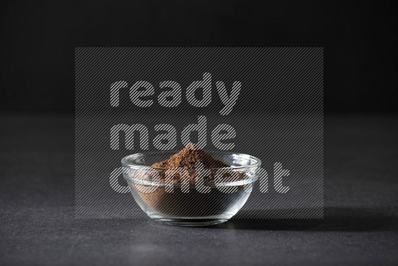 A glass bowl full of cloves powder on black flooring