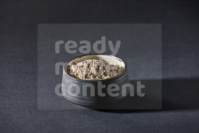 وعاء فخار أسود مملوء بالفلفل الأبيض على أرضية سوداء