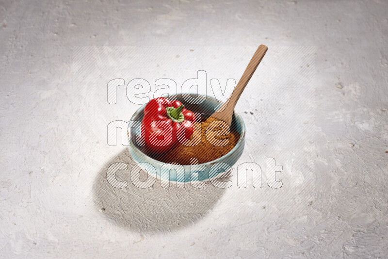 A colored pottery plate full of ground paprika powder and red bell pepper on white background