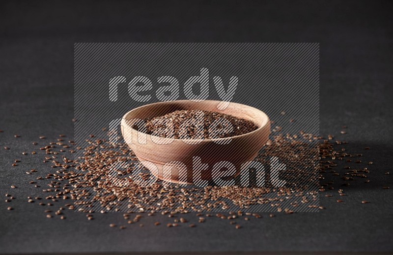 A wooden bowl full of flax surrounded by the seeds on a black flooring in different angles
