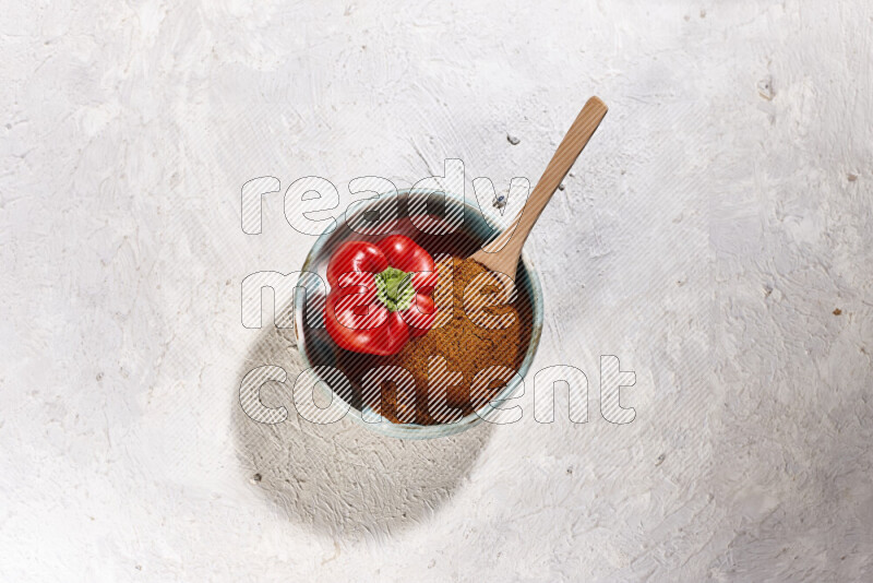 A colored pottery plate full of ground paprika powder and red bell pepper on white background