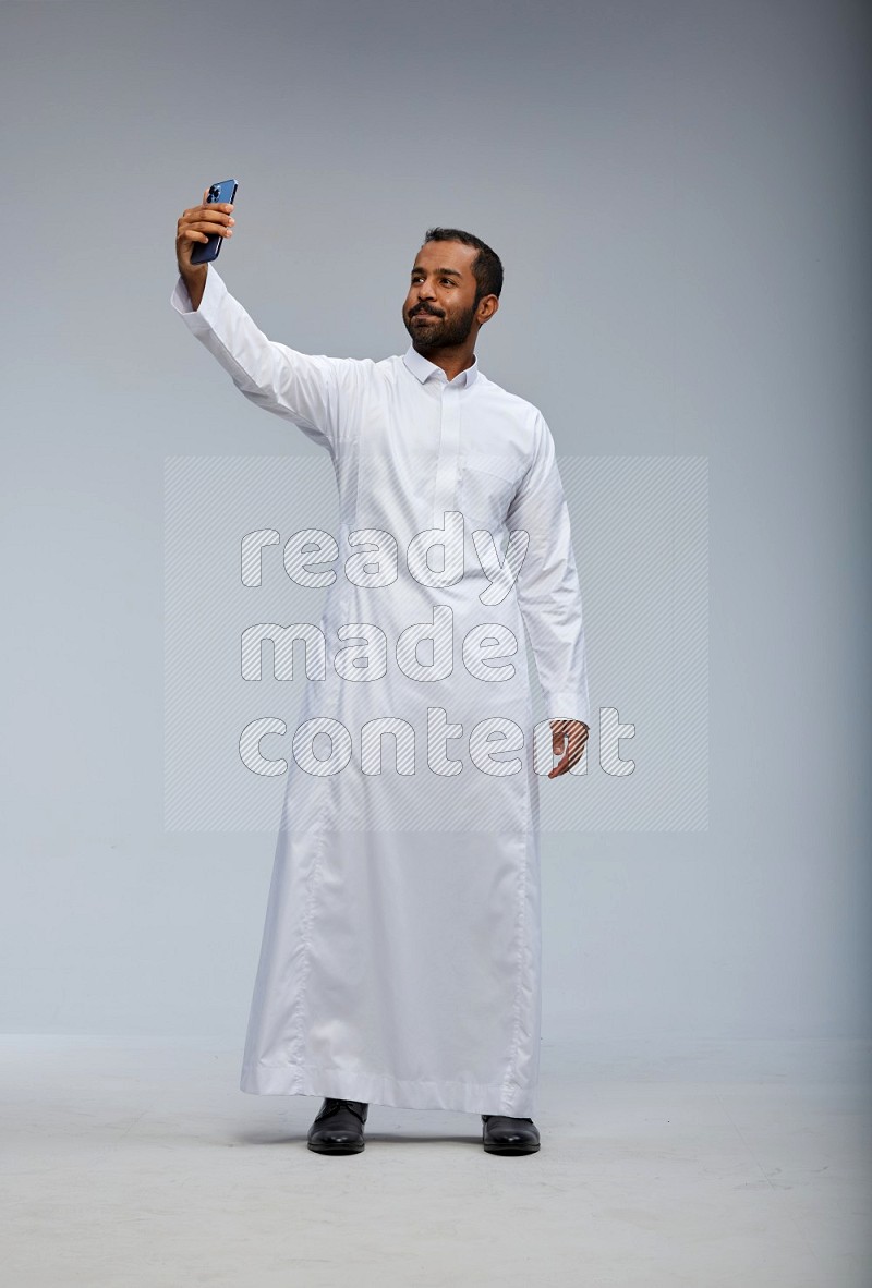 Saudi man wearing Thob standing taking selfie on Gray background