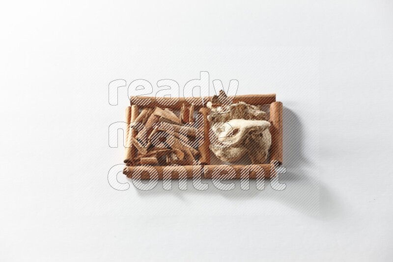 مربعان من أعواد القرفة ممتلئان بقطع من القرفة والزنجبيل المجفف علي خلفية بيضاء