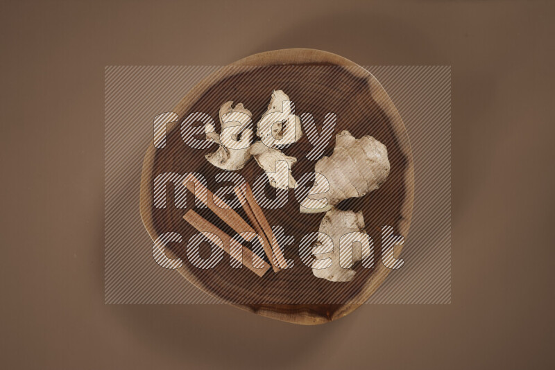 An assorted whole spices on a flat wooden tray including fresh and dried ginger, cinnamon sticks, cardamom, turmeric fingers, cloves, star anise on beige background