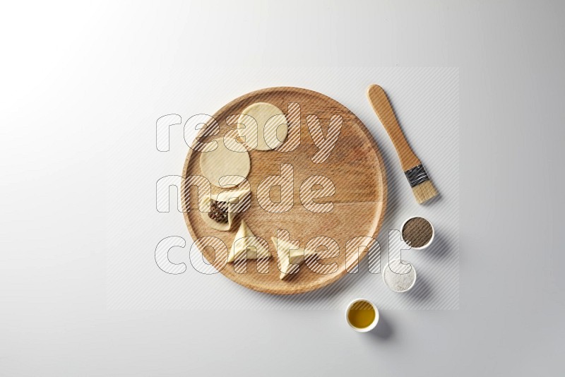 two closed sambosas and one open sambosa filled with meat while salt, black pepper and oil with oil brush aside in a wooden dish on a white background
