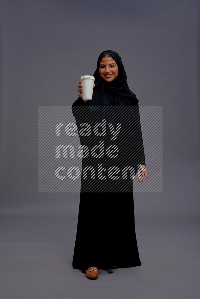 Saudi woman wearing Abaya standing holding paper cup on gray background