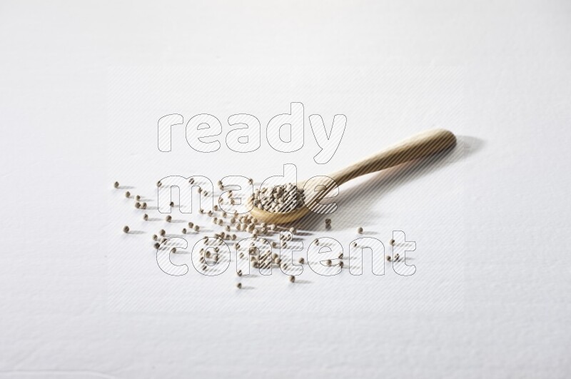 A wooden spoon full of white pepper beads on white flooring