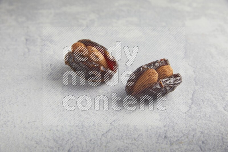 two almond stuffed madjoul dates on a light grey background
