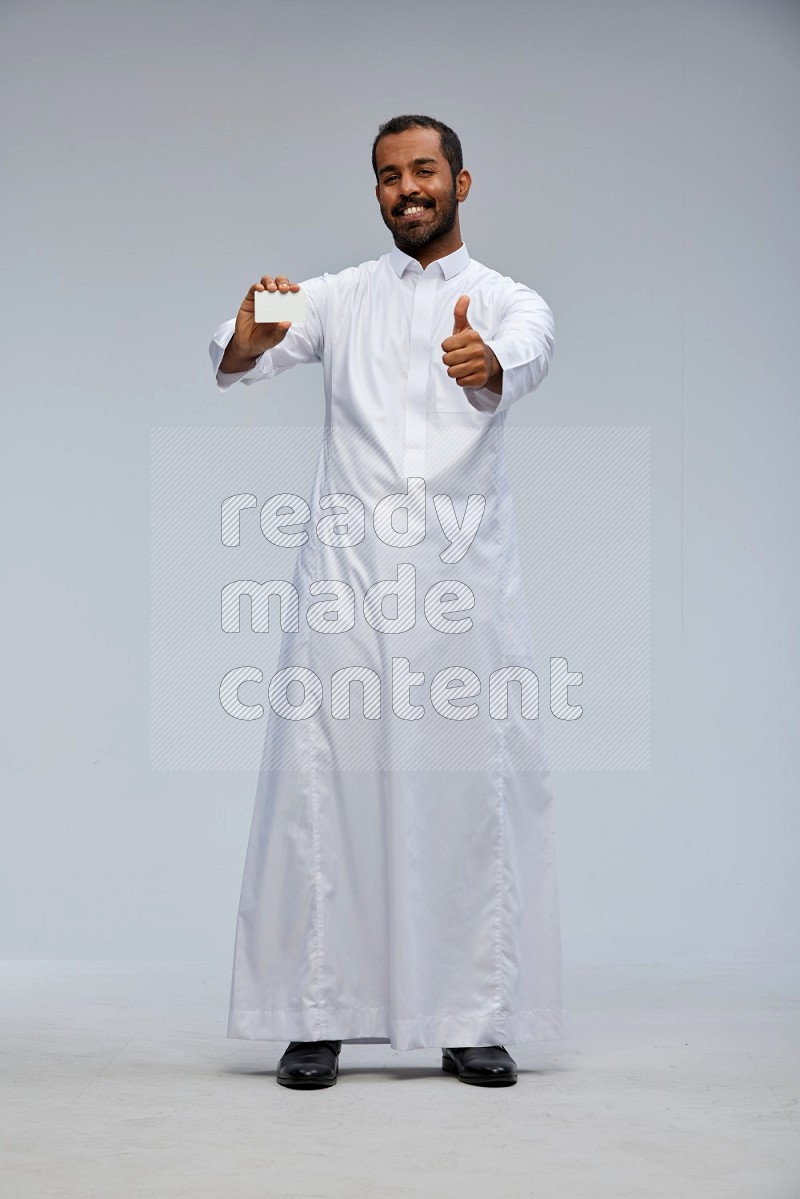 Saudi man wearing Thob standing holding ATM card on Gray background