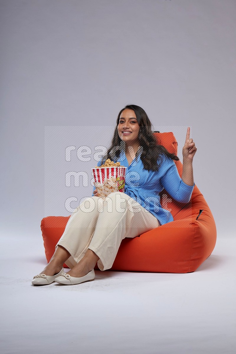 A woman sitting on an orange beanbag and eating popcorn