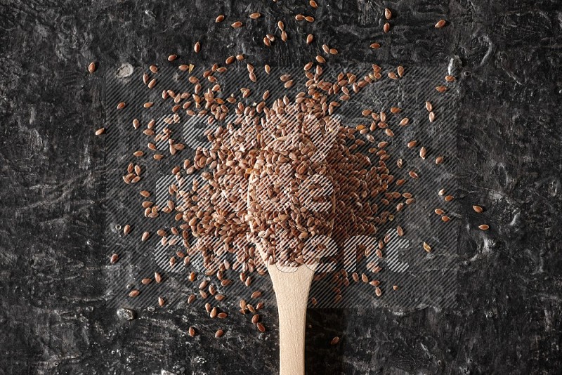 ملعقة خشبية ممتلئة بحبوب بذر الكتان محاطه بالبذور علي خلفية سوداء