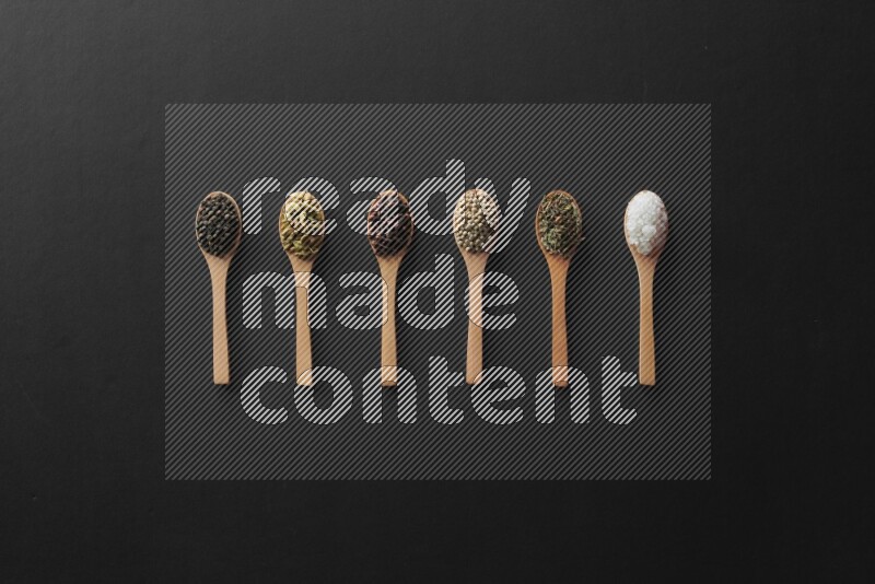 الفلفل الأبيض والقرنفل والهيل والملح والفلفل الأسود وريحان مجفف في معالق خشبية علي خلفية سوداء