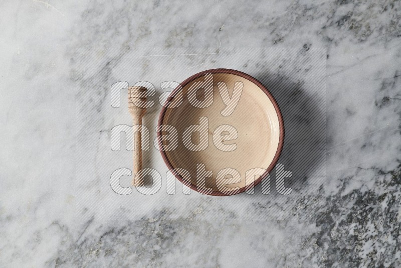 Beige Pottery Oven Bowl Plate with wooden honey handle on the side on grey marble flooring, Top view