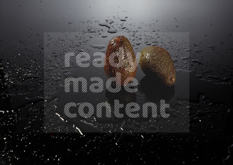 A whole avocado on black background with water drops.