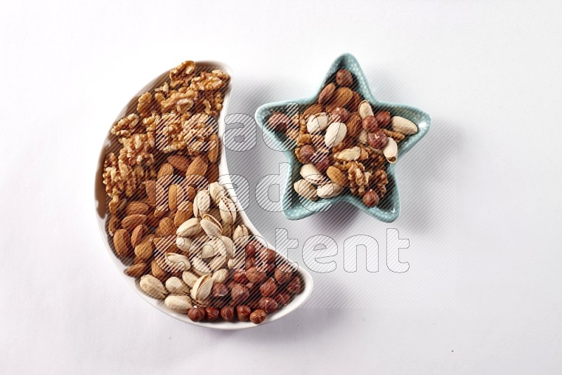 Mixed nuts in a crescent pottery plate and a star shaped plate on white background